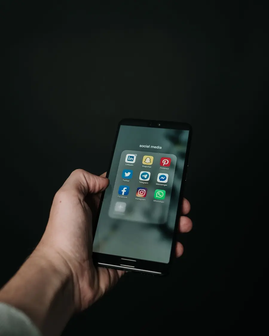 A hand holding a phone showing social apps in a dark room.