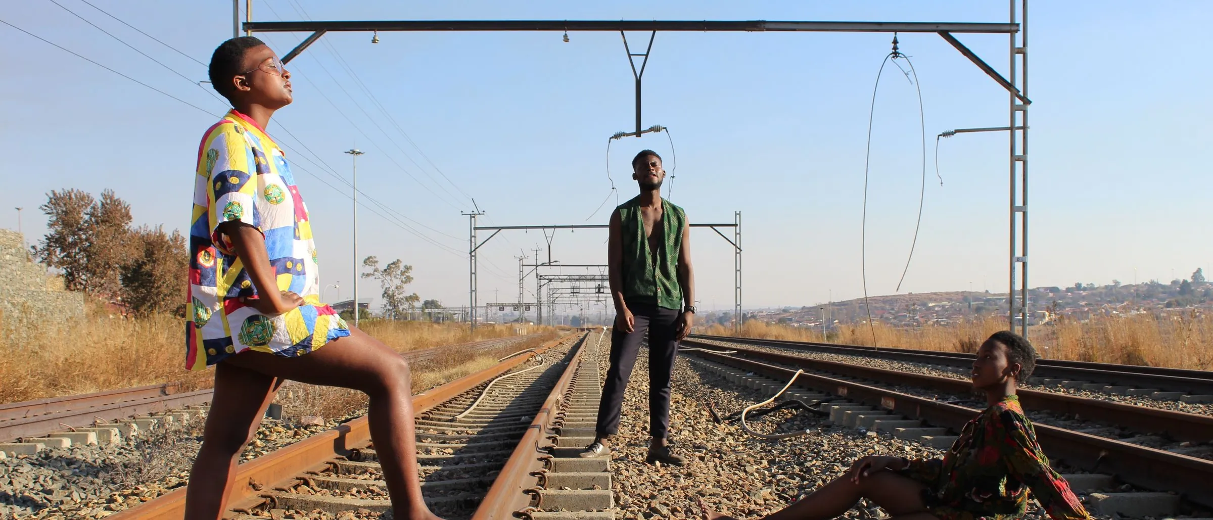Three young people in bold printed outfits posing on railway tracks in Soweto.
