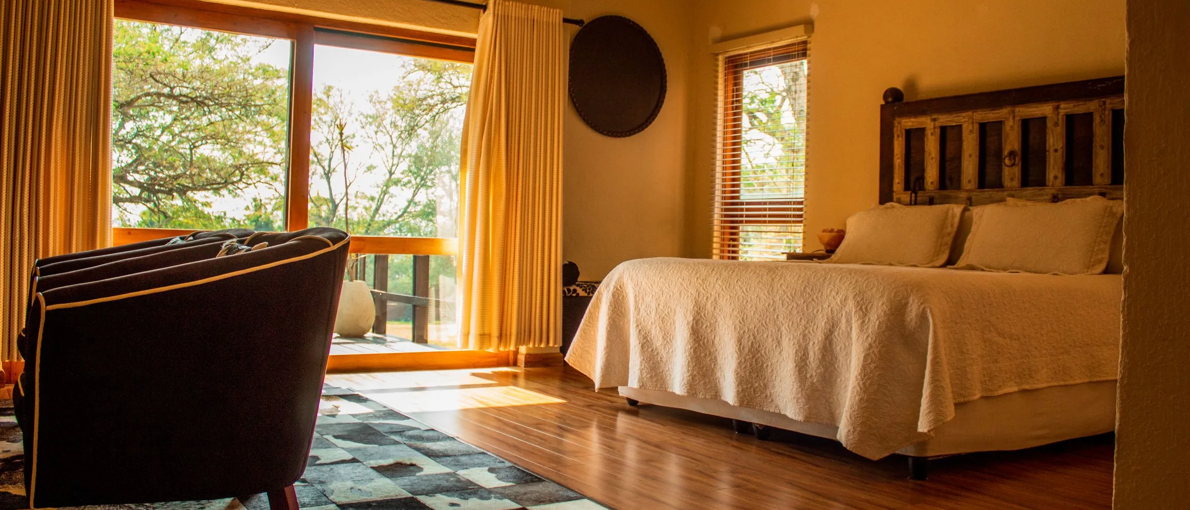 A warm lodge bedroom in South Africa, with a leather chair and doors open to the trees.