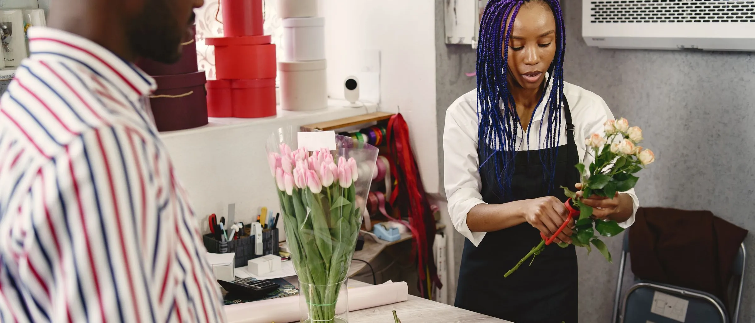 A florist arranging a bouquet of roses for a customer at her shop counter.
